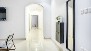 A hallway with a flat-screen TV mounted on the wall, a chair, and a potted plant. - Badrani A - Qaswarah Residence  (Madinah)