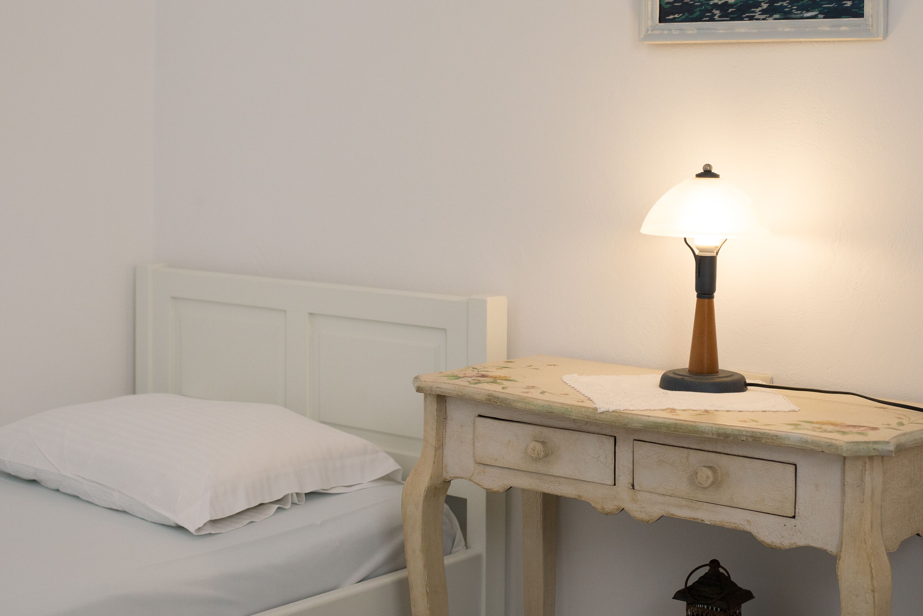Een kleine, witte eenpersoonskamer met nachtkastje en lamp.