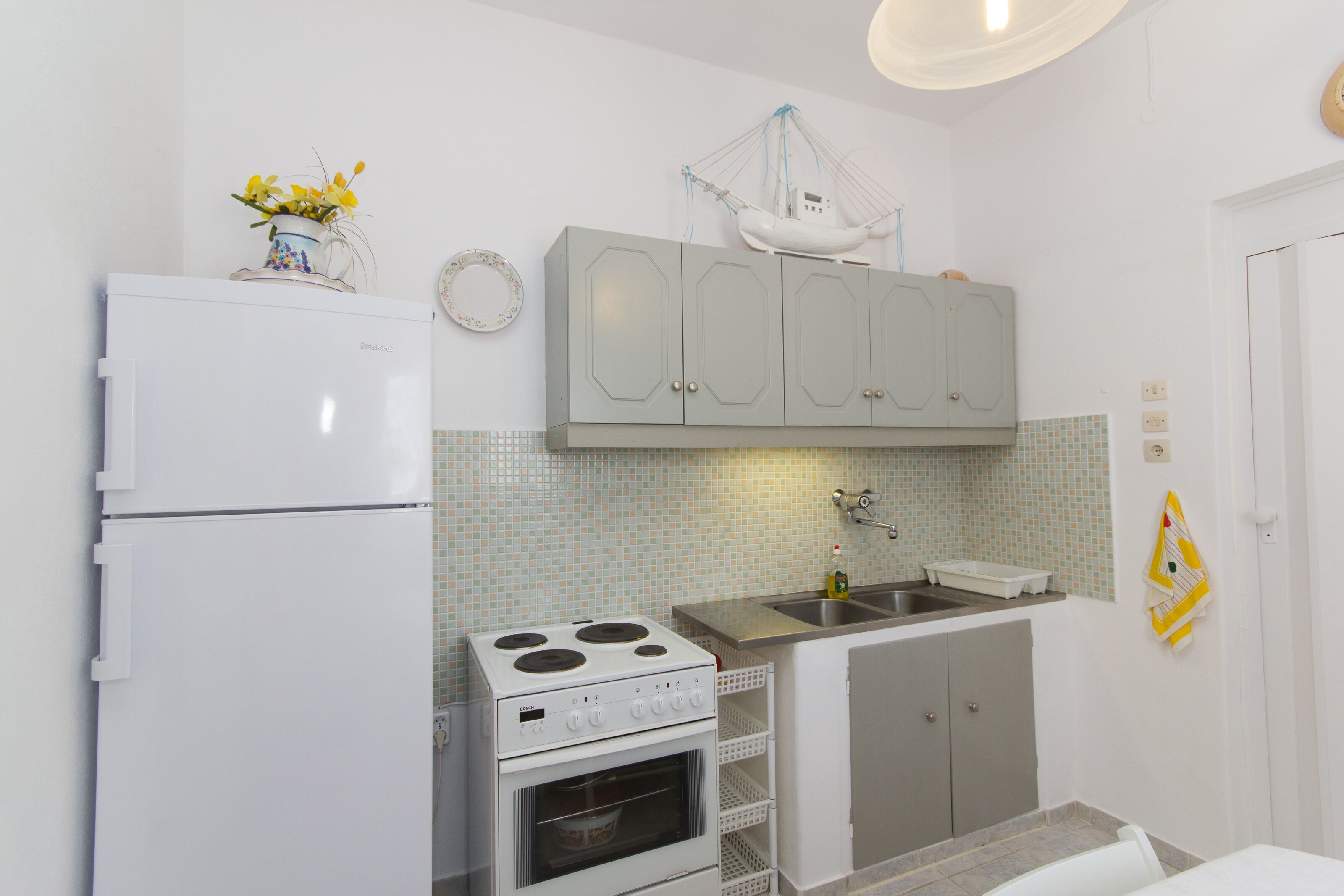 Una cocina compacta con refrigerador, estufa, pileta y gabinetes grises.