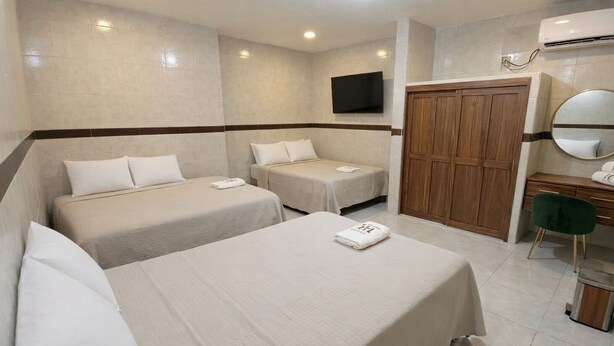 Habitación de hotel con dos camas, un escritorio con silla, un armario y un televisor montado en la pared.