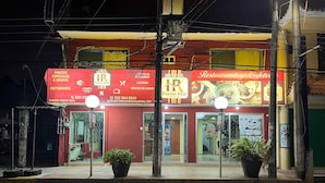 Un hotel con fachada roja, un letrero que dice 'Hotel Puerto Real' y un letrero de 'Restaurante Café'. Hay dos plantas en macetas frente a la entrada.