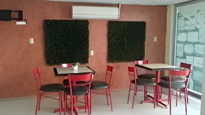 Una habitación con dos adornos verdes en la pared, un equipo de aire acondicionado blanco y una mesa con cuatro sillas rojas.