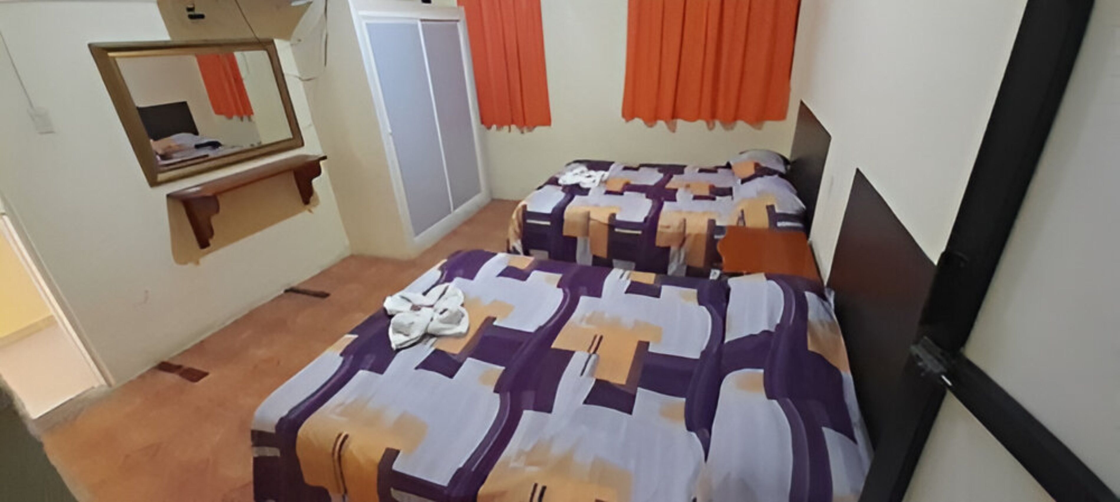 A bedroom with a bed, a wardrobe, a mirror, and orange curtains.