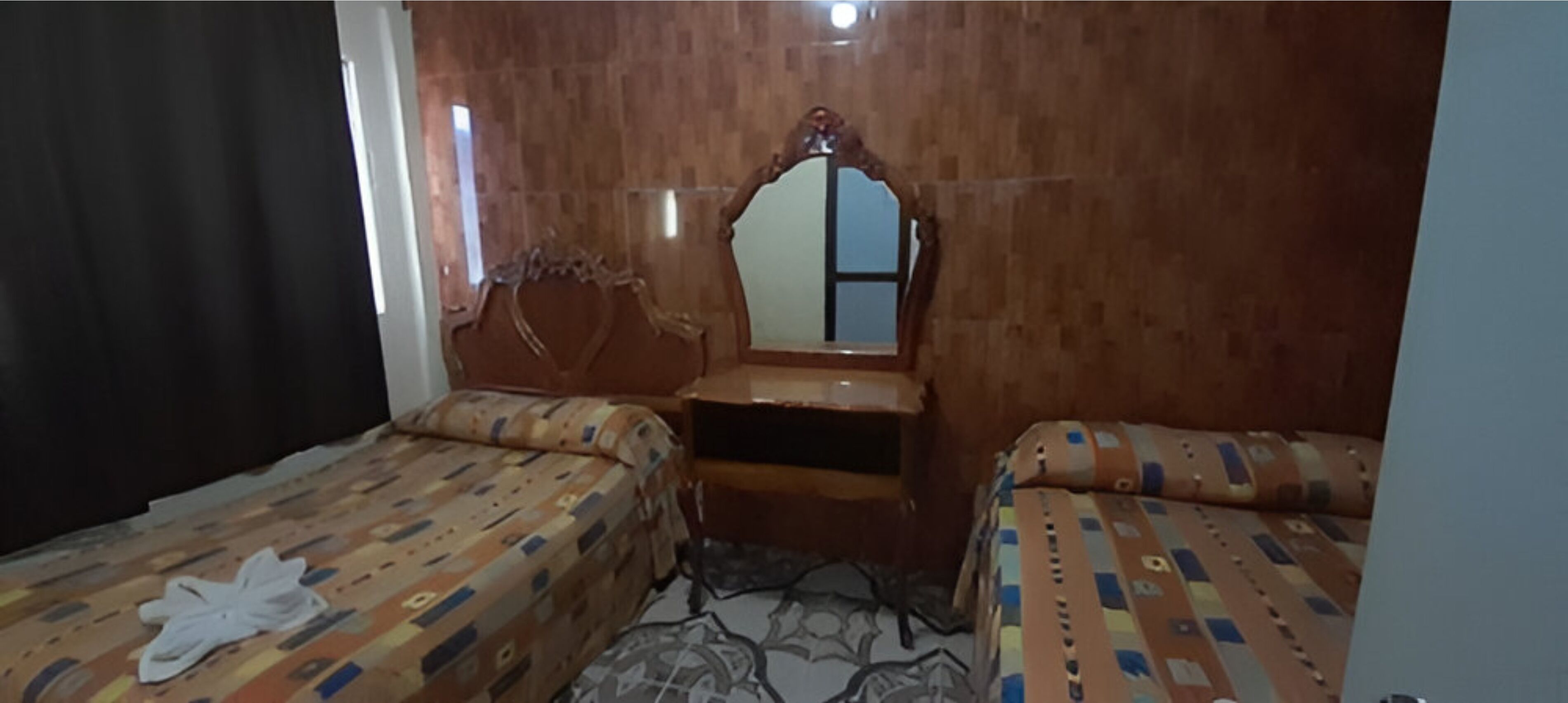 Una habitación con dos camas, cabecero de madera, un espejo y una mesita.