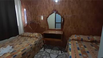 Una habitación con dos camas, cabecero de madera, un espejo y una mesita.