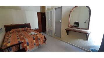 Une chambre à coucher avec un lit, une armoire, un miroir et une petite table.