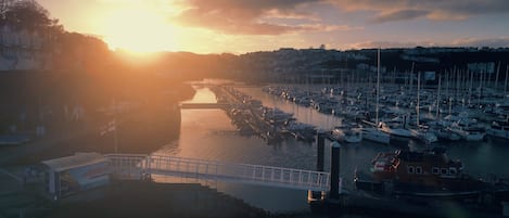 A marina with boats docked, a bridge, and buildings along the waterfront.
