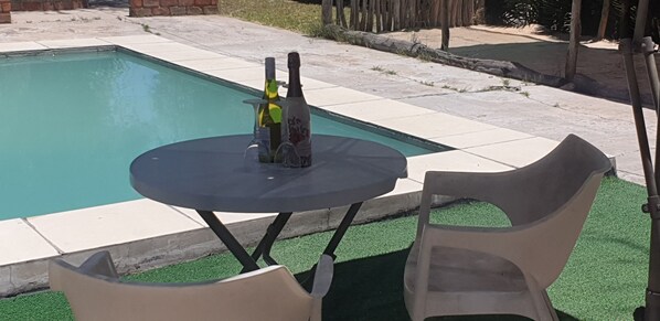 A poolside area with a table and two chairs, a bottle of wine, and a glass.
