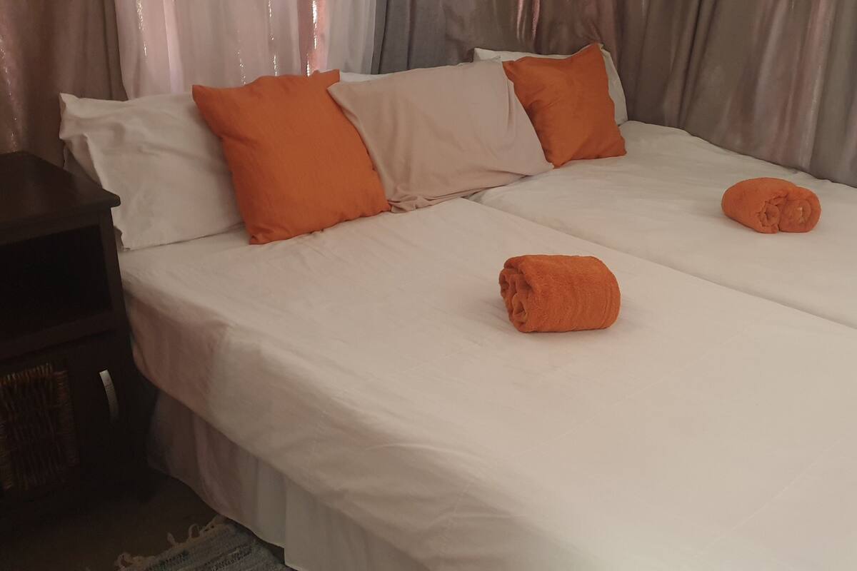 A double bed with white bedding and two orange pillows.