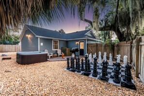 A house with a backyard containing a large chessboard and a hot tub.