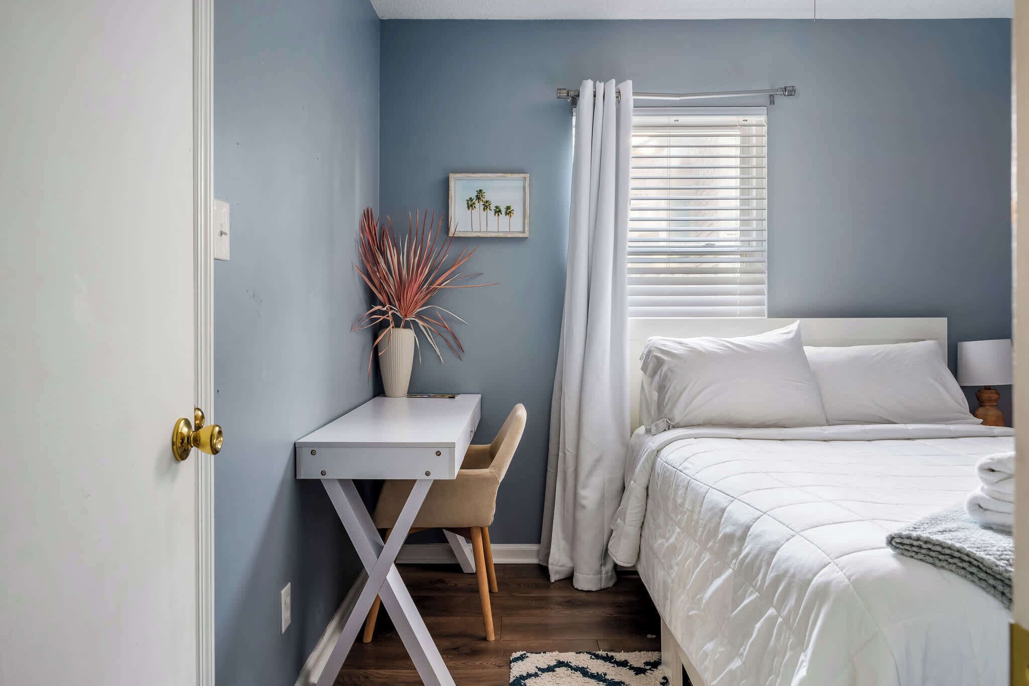 Une chambre à coucher avec un lit, un bureau, une chaise et une fenêtre avec des rideaux.