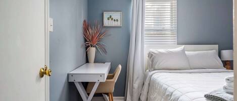 Une chambre à coucher avec un lit, un bureau, une chaise et une fenêtre avec des rideaux.