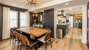 A modern kitchen with a central island, a dining area with a wooden table and chairs, and a view into the adjacent living space.