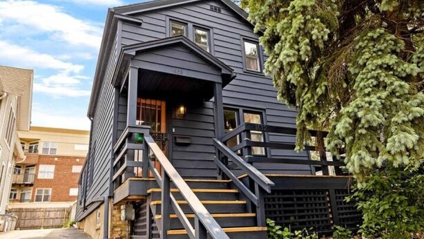 A modern two-story building with a dark exterior, a wooden staircase, and a small porch area.