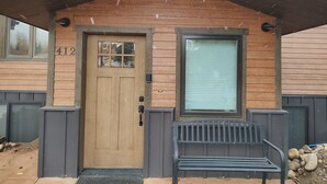 Une maison en bois avec le numéro 412 sur la porte, une fenêtre avec des stores et un banc à l’extérieur.