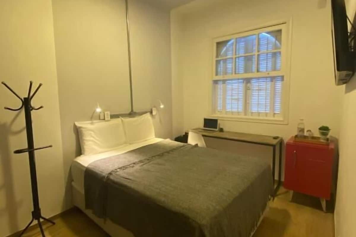 A bedroom with a bed, a window, a desk, and a red cabinet.