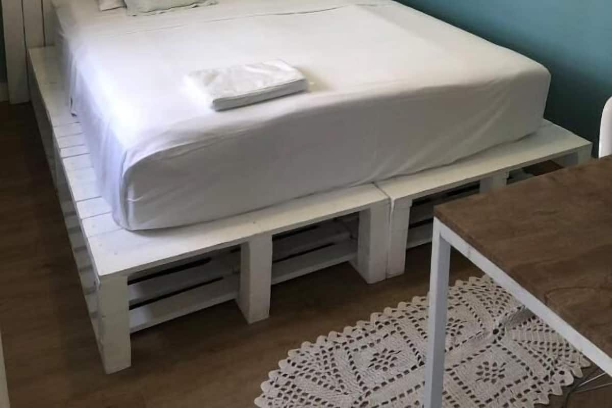 A single-bed room with a wooden bed frame, white bedding, and a small table with a doily.
