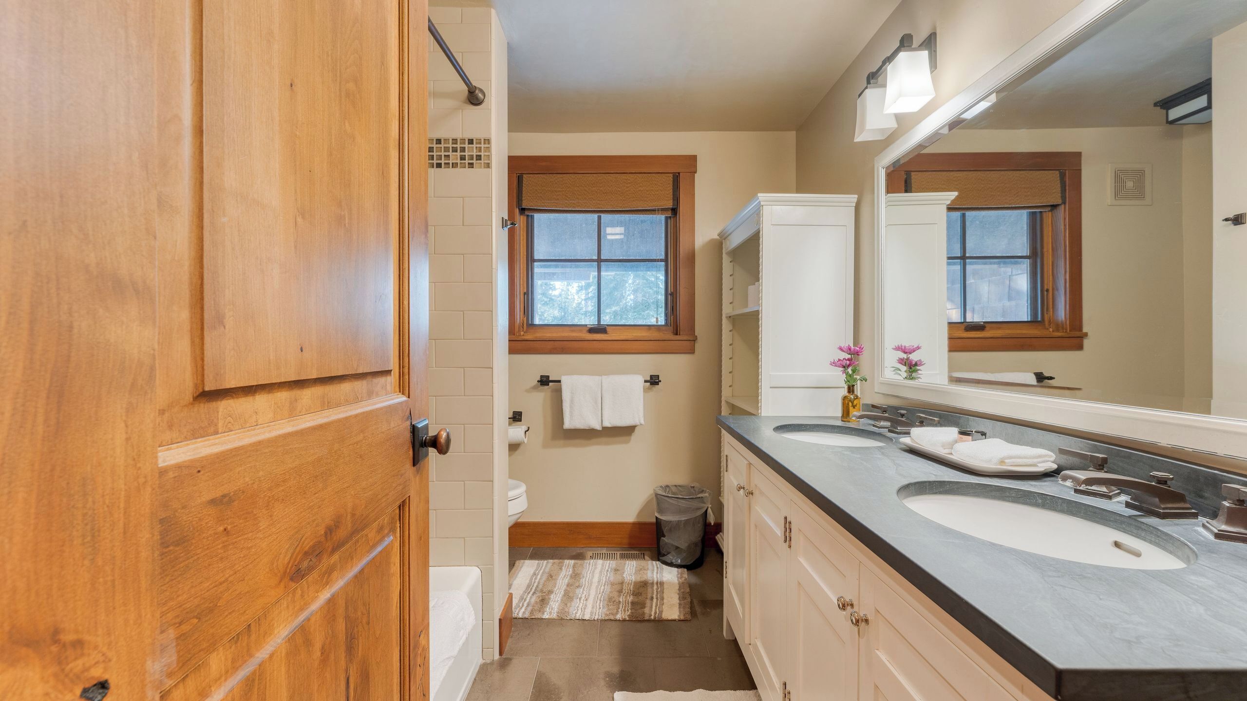 A bathroom with a wooden door, a window, a sink, and a mirror.