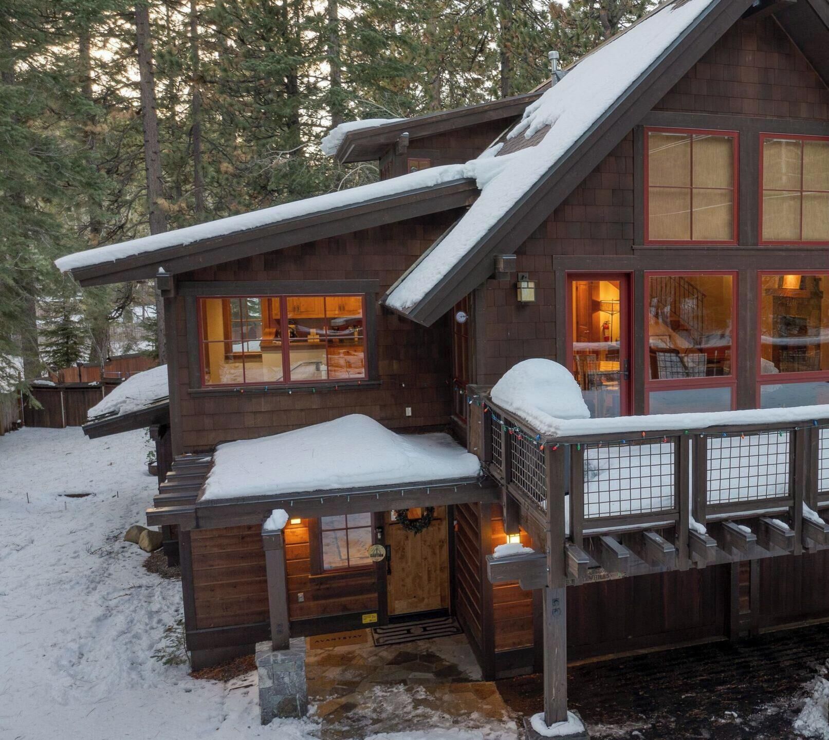 A cabin with a deck, large windows, and a snow-covered roof.
