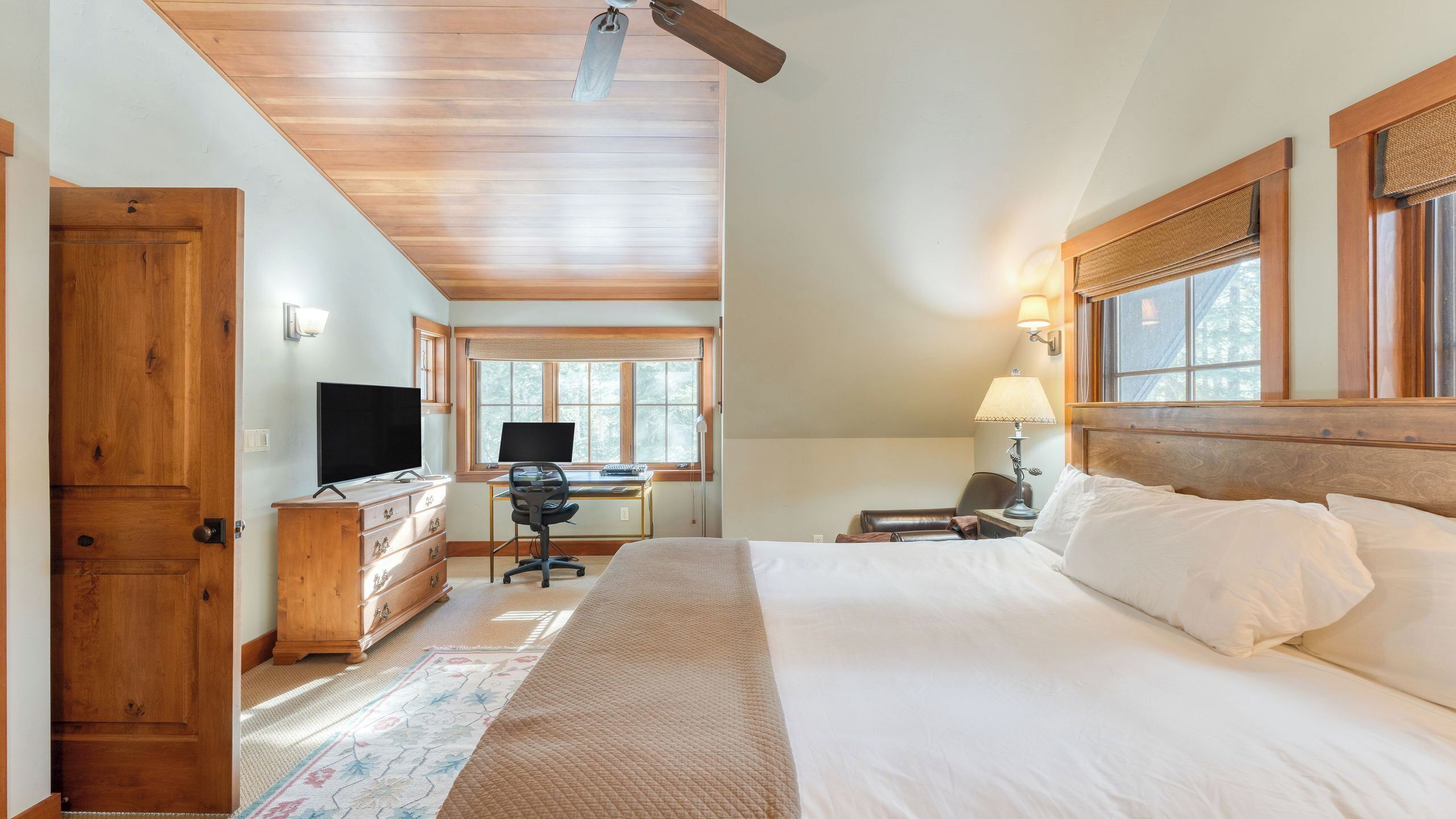 Een slaapkamer met een bed, bureau, stoel, televisie en een raam met jaloezieën.