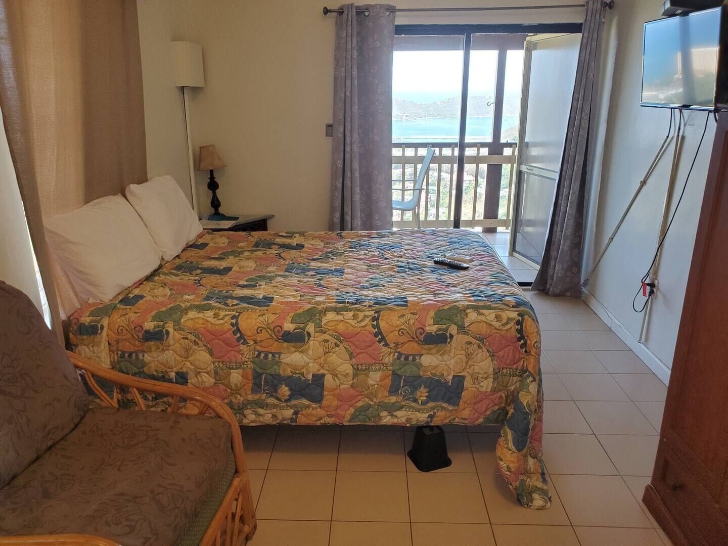 A hotel room with a bed, a chair, a TV, and a balcony with a view.