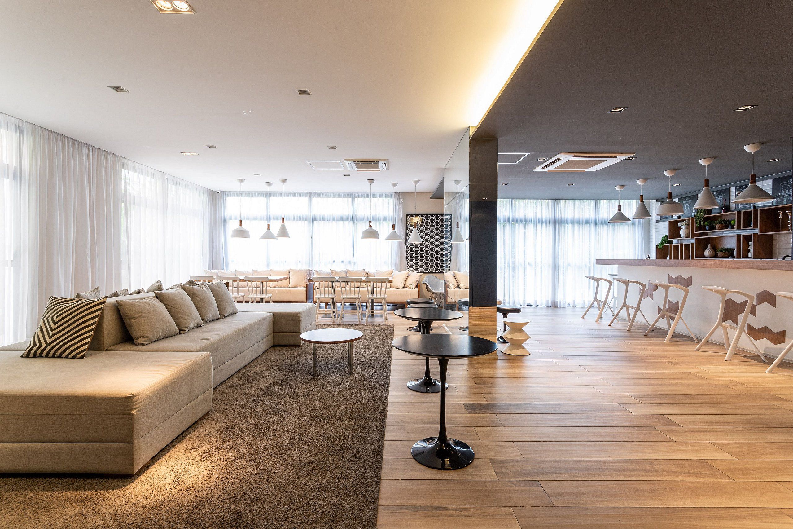 A modern living room with a sofa, coffee table, and chairs. There is a kitchen area with a bar and shelves.
