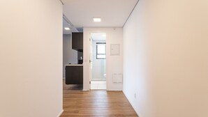 A narrow hallway with wooden flooring leading to a kitchen area with a dark countertop and a white door. - Setin Downtown Genebra by Viva - Apartamentos completos na Bela Vista com piscina (São Paulo)