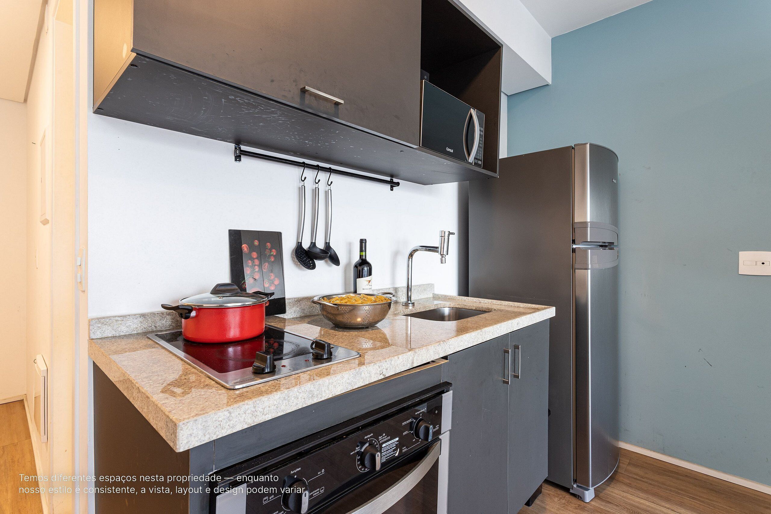 A compact kitchen with a stainless steel refrigerator, a red pot on the stove, and a bowl of food on the counter.