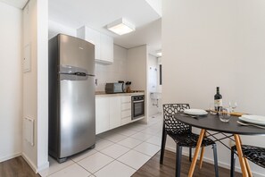 A modern kitchen with a stainless steel refrigerator, a built-in oven, and a microwave. There is a dining table with chairs and a wine bottle on it.