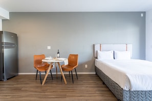 Quarto de hotel com cama, mesa de jantar para duas pessoas, geladeira e um interruptor de luz na parede.