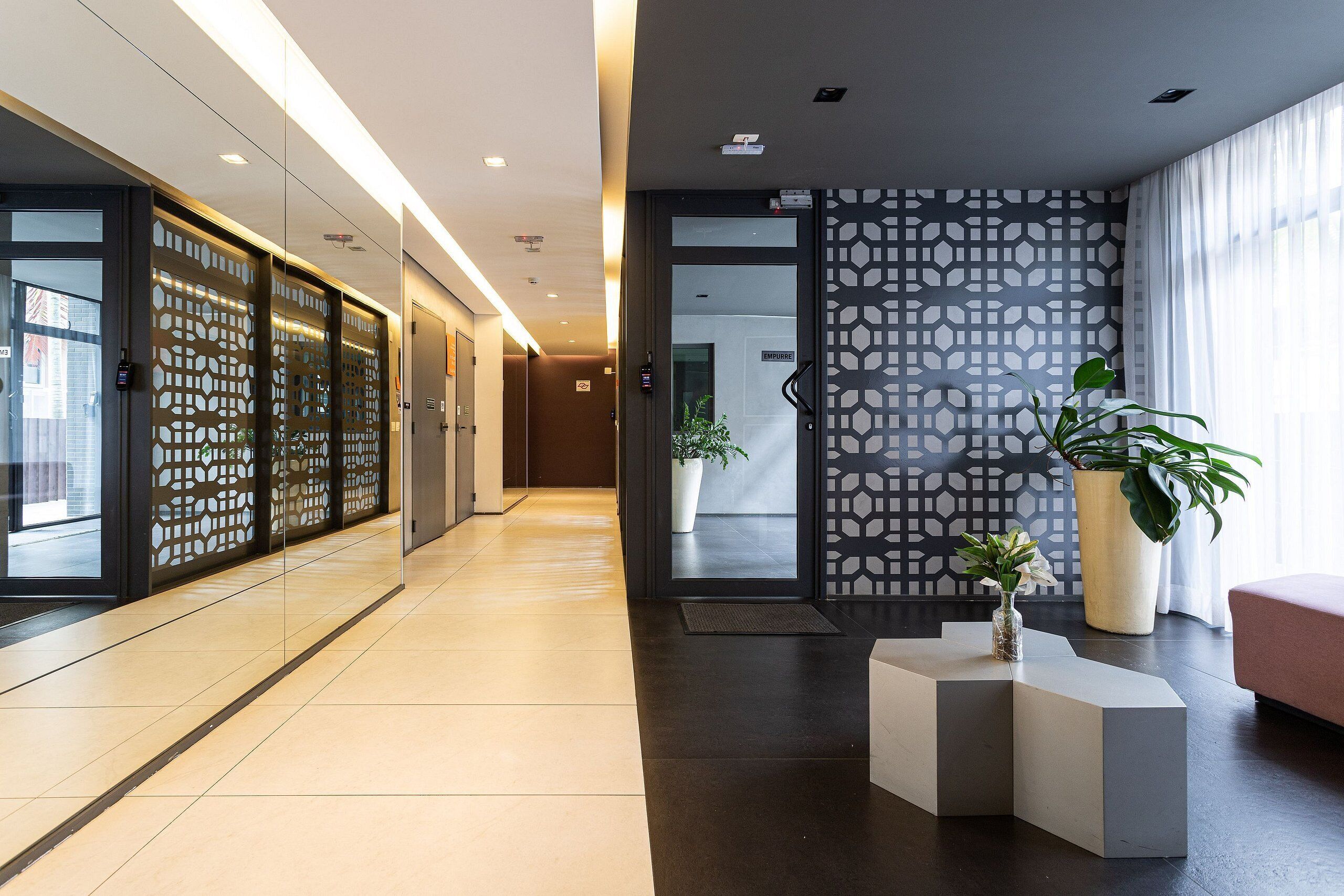 Un hall d’hôtel moderne avec un long couloir, un comptoir d’accueil et une grande plante en pot.
