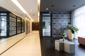 Un hall d’hôtel moderne avec un long couloir, un comptoir d’accueil et une grande plante en pot.