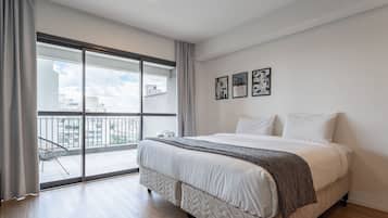 A bedroom with a large bed, a view of the city through a sliding glass door, and three framed pictures on the wall.