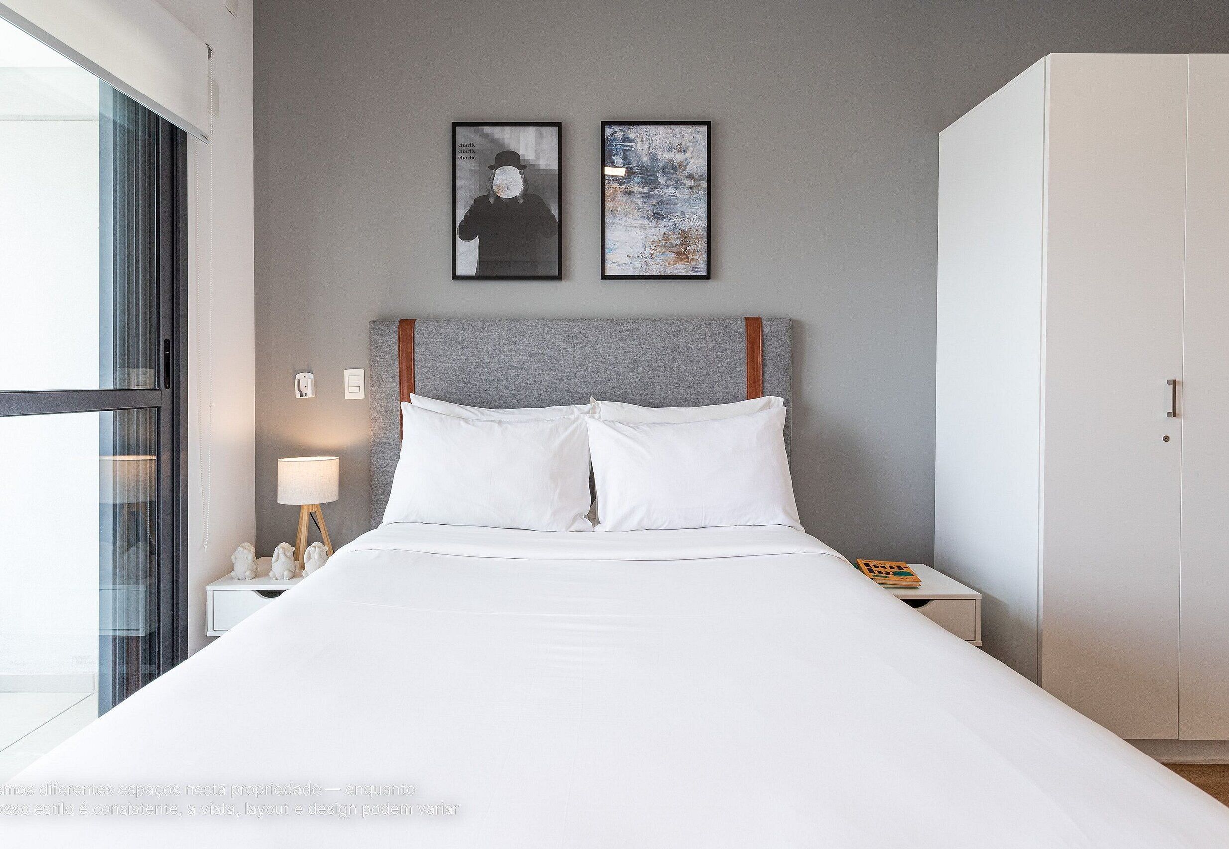 A neatly made bed with white linens, a bedside lamp, and two framed pictures on the wall.