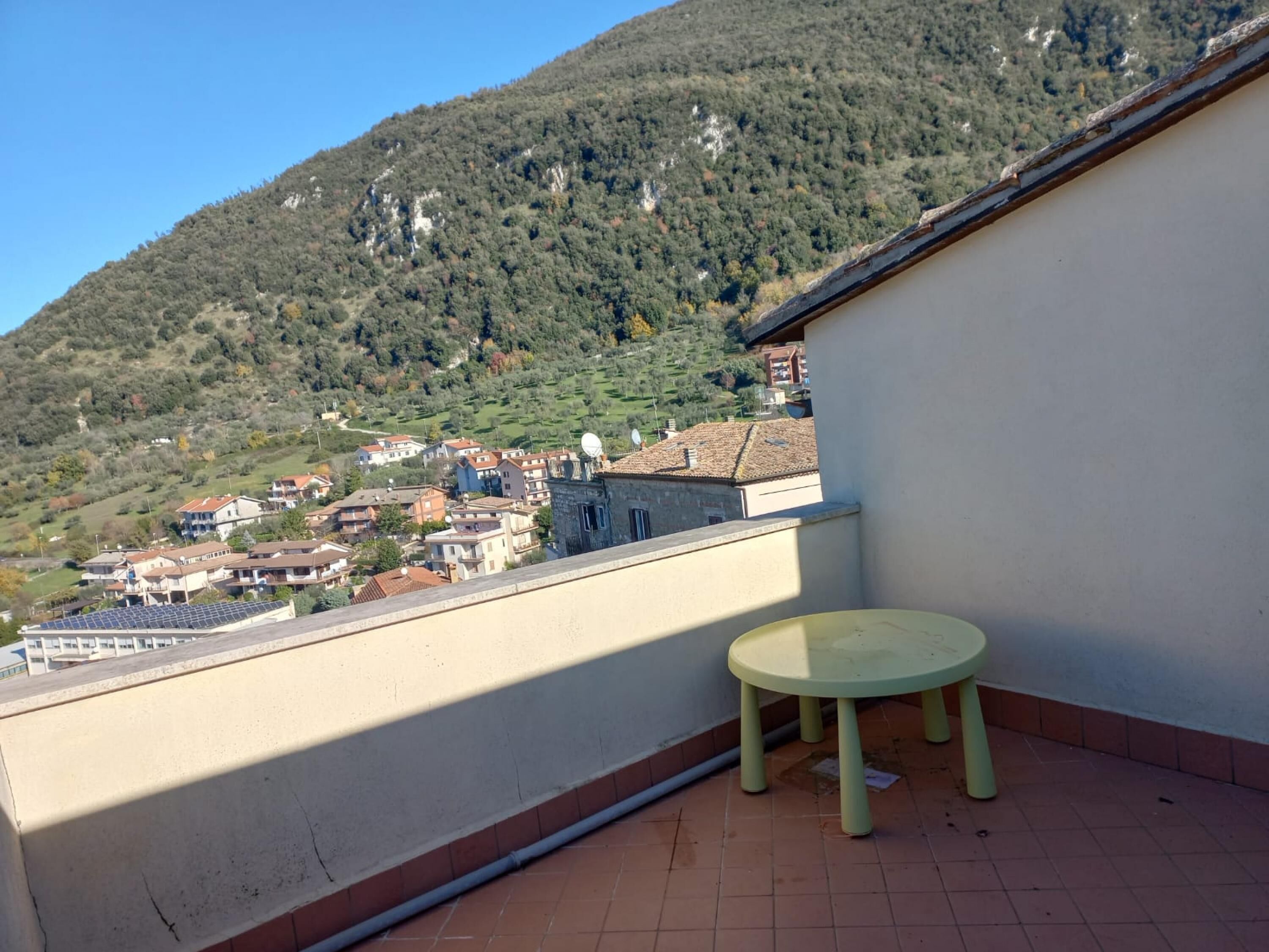 A balcony with a view of a hillside village, a small table, and a tiled floor.