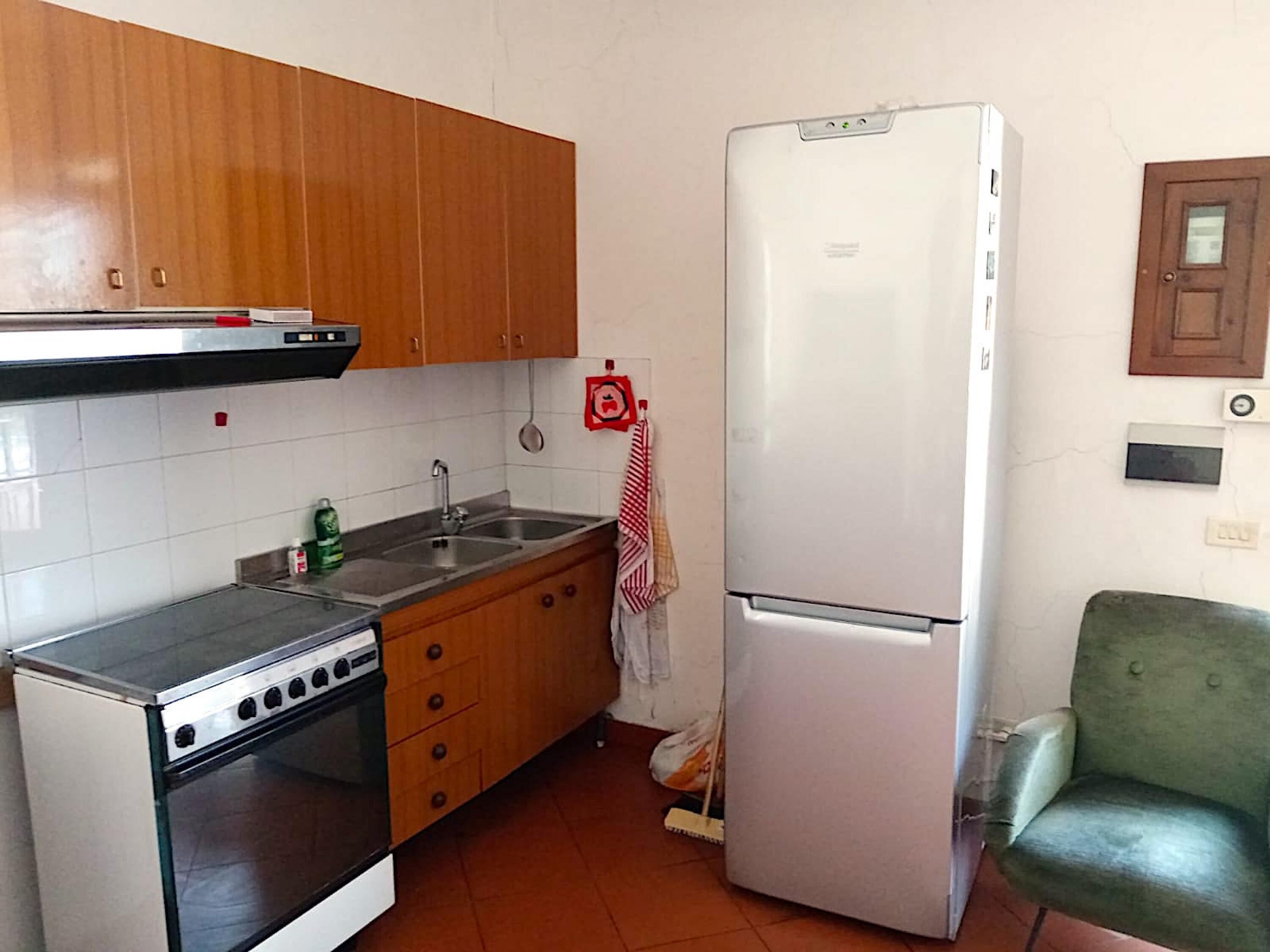 Une cuisine de taille réduite, dotée de meubles en bois, d’une cuisinière en acier inoxydable, d’un évier et d’un réfrigérateur blanc.