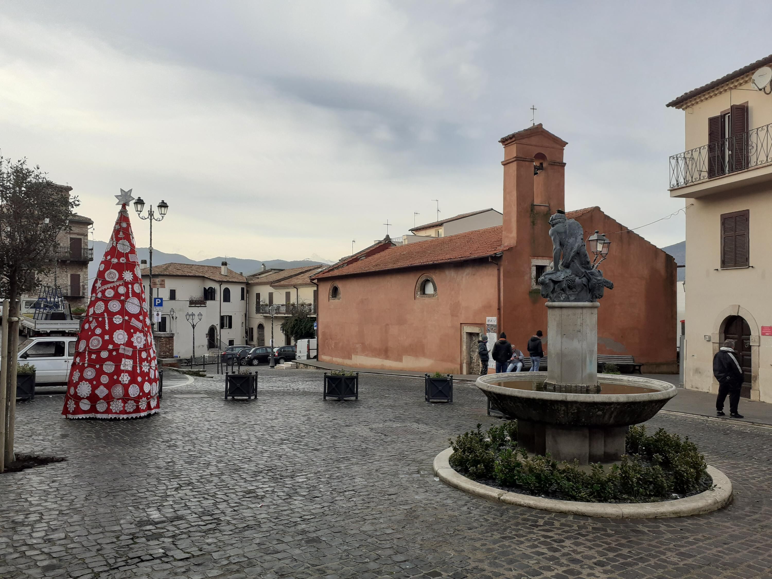 A cobblestone square with a fountain, a church, and a statue.