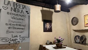 Ein rustikaler Innenraum mit einem Schild, das verschiedene Willkommensbotschaften in verschiedenen Sprachen zeigt, einer Holzbalkendecke, einem Tisch mit einer floralen Dekoration und einem an der Wand hängenden Bild.