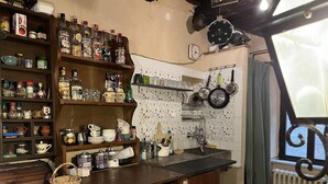 Eine Küche mit Holzböden, gefüllt mit Flaschen, Gläsern und Küchenutensilien. Es gibt ein Waschbecken mit Armatur, ein Fenster mit Vorhängen und eine Heizung.