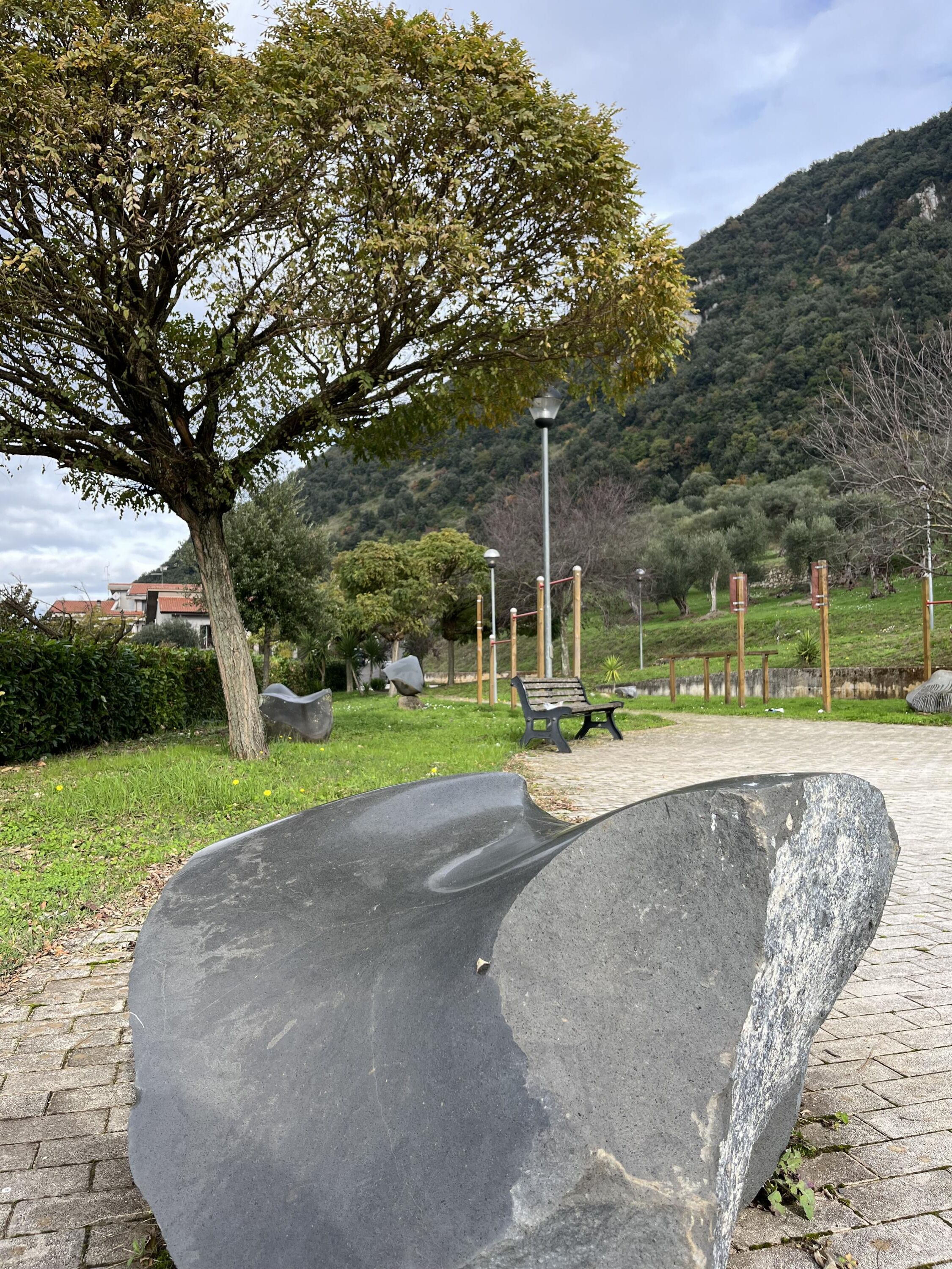 A park with a large stone sculpture, benches, and a tree.