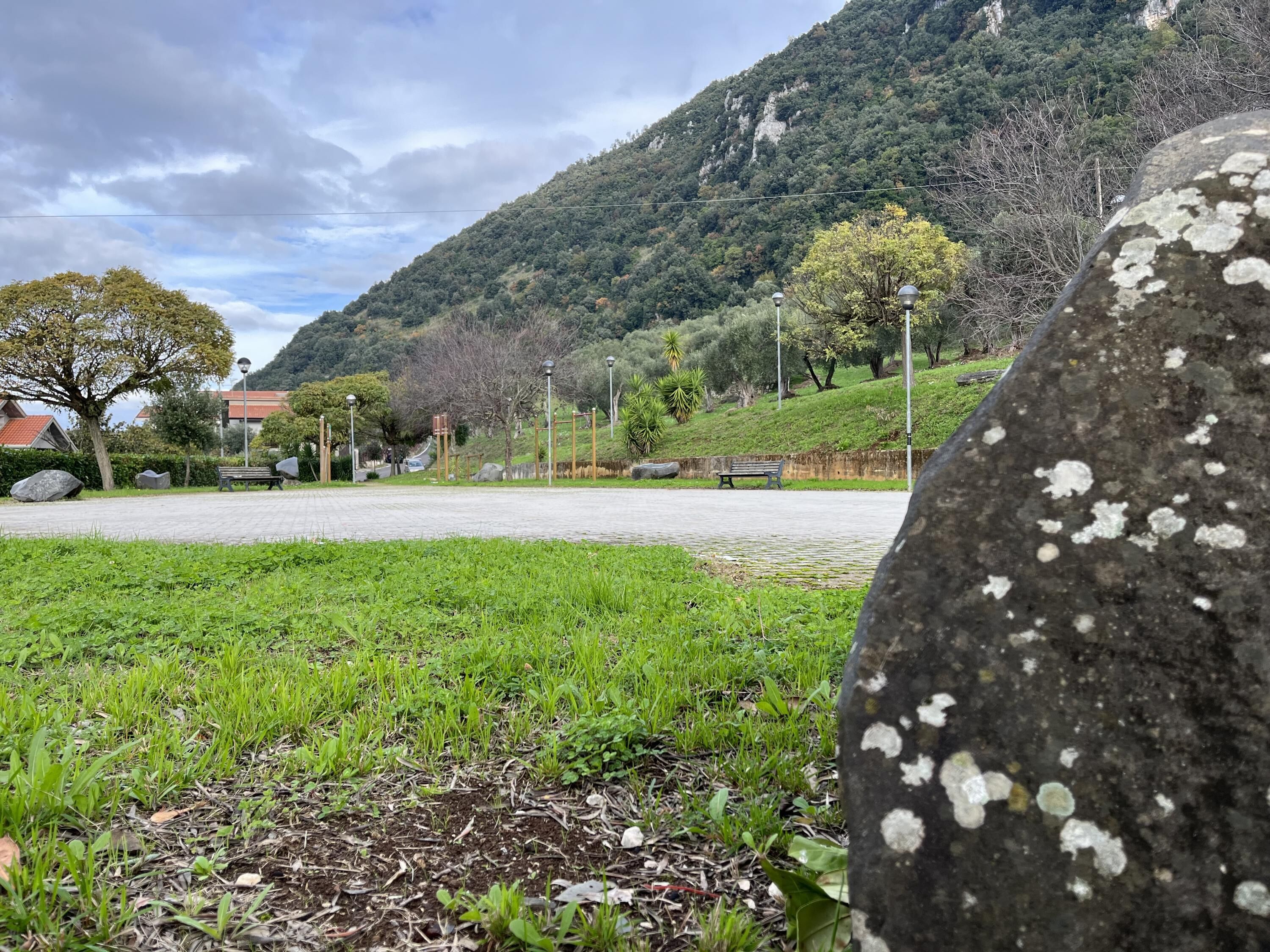 A paved pathway with benches, a grassy area, and a mountain in the background.