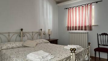 Un dormitorio con cama, mesita de noche, lámpara, silla y ventana con cortinas.