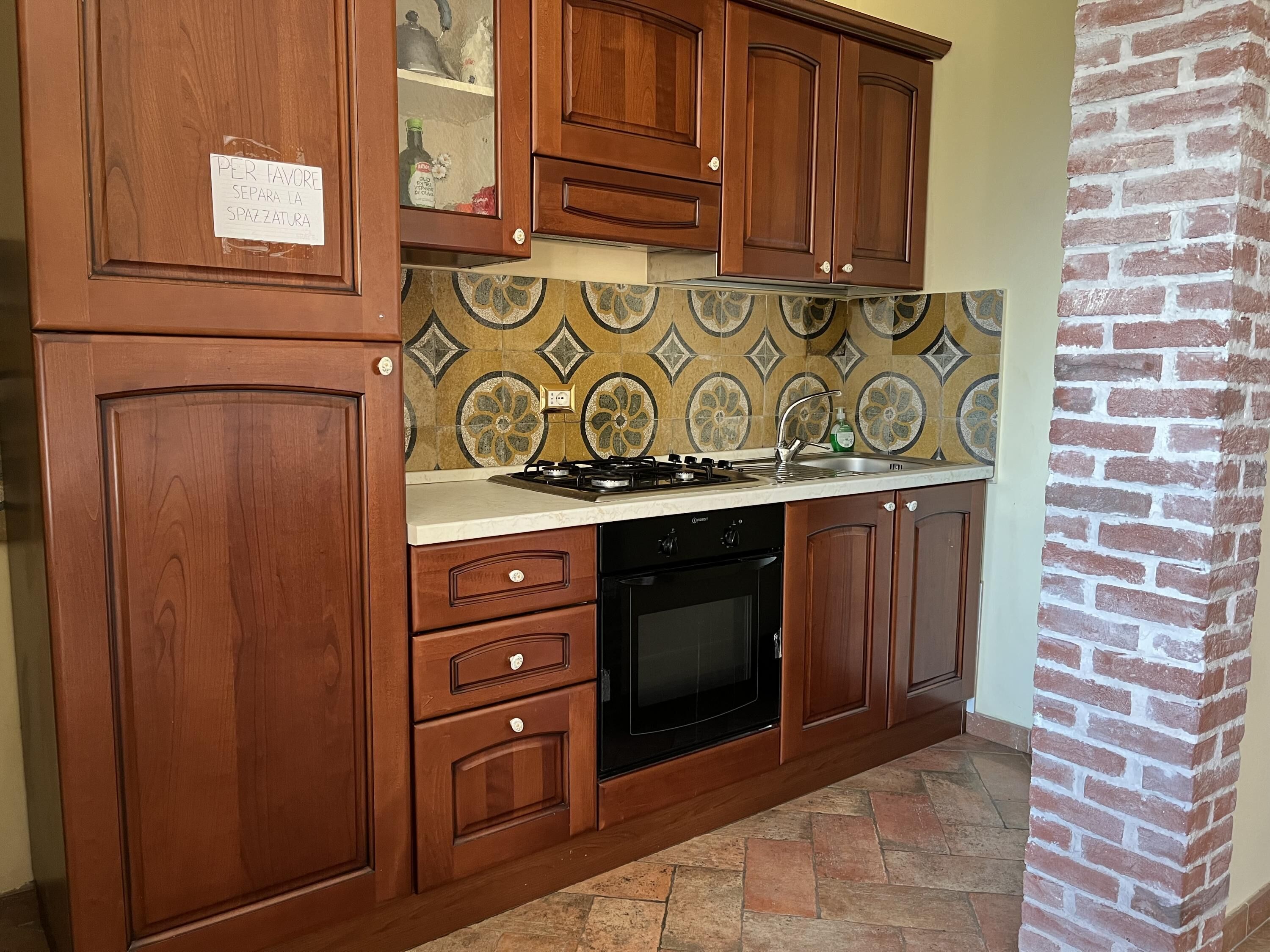 Une cuisine avec des meubles de rangement en bois, une cuisinière à gaz, un évier et des carreaux décoratifs sur le mur derrière l’évier.