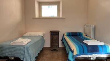 Ein kleines, sauberes Zimmer mit zwei Betten, einem Fenster, einem Heizkörper und einem Holzschrank.