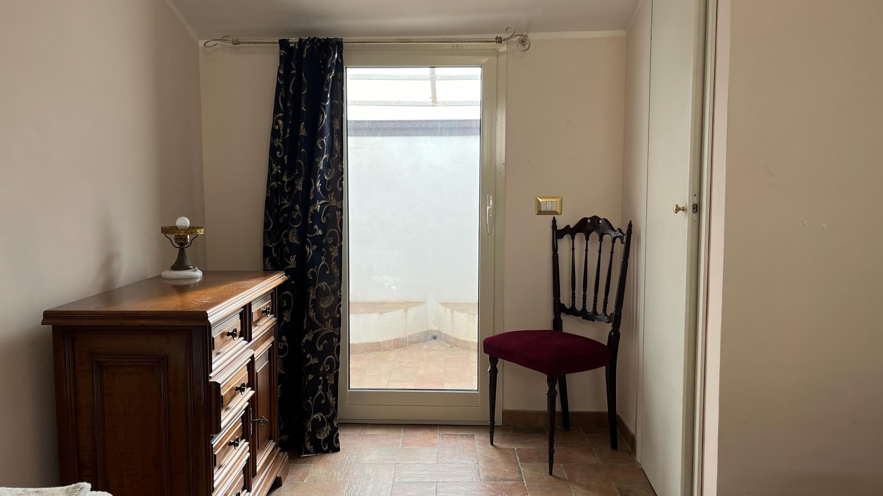 A room with a wooden desk, a chair, a curtain, and a door leading to an outdoor area.