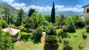 A lush garden with a variety of plants and trees, a stone pathway, and a building with a balcony. - Villa Felici Montecristo (Giuliano di Roma)