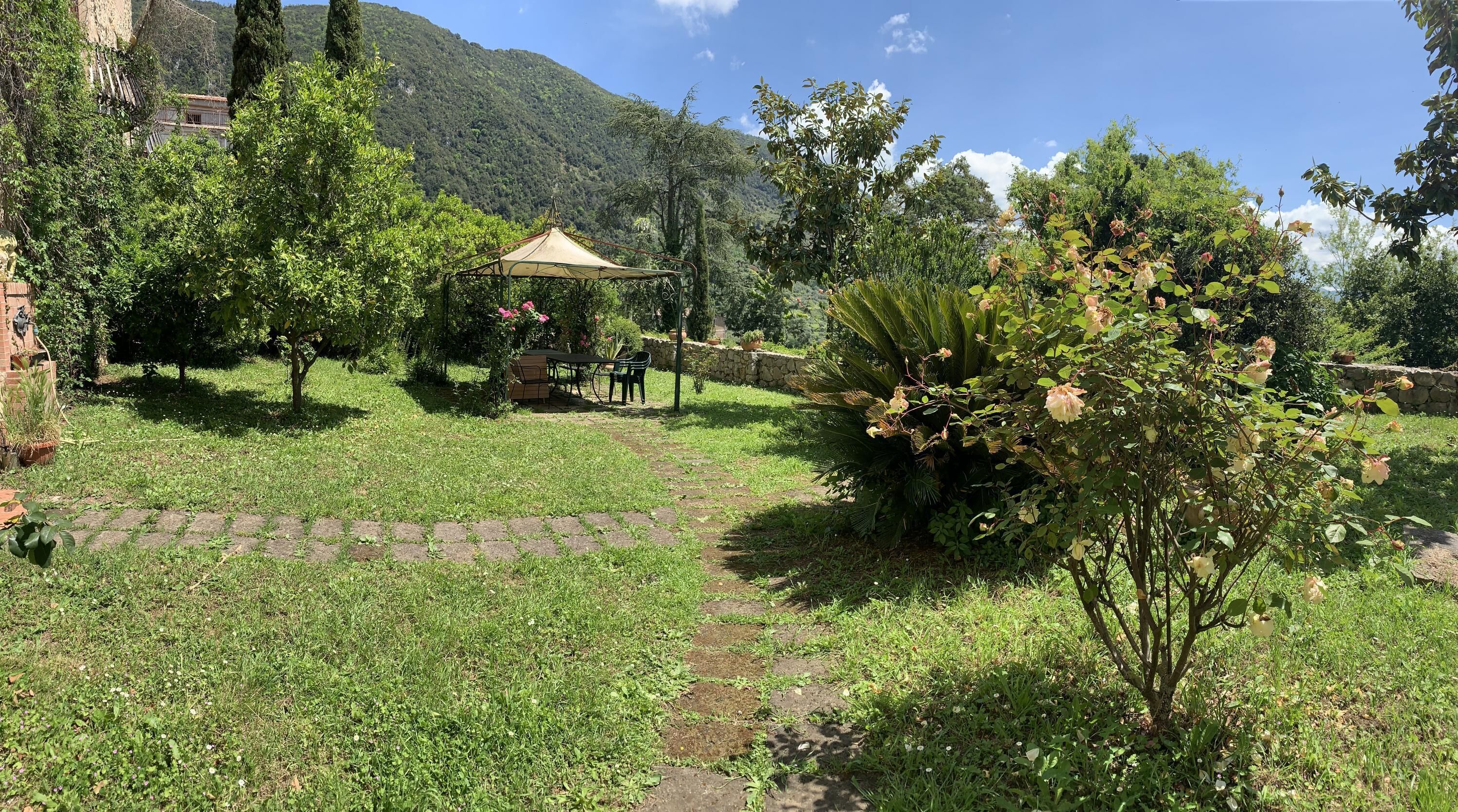 A garden with a gazebo, stone wall, and a mountain in the background.