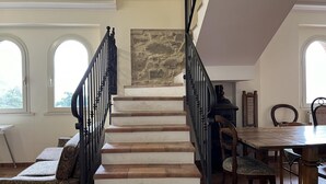 A staircase with stone walls, a dining area with wooden furniture, and large windows. - Villa Felici Montecristo (Giuliano di Roma)