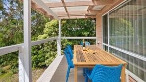 Ein überdachter Außenbereich mit Holztisch und blauen Stühlen, umgeben von Grünpflanzen.