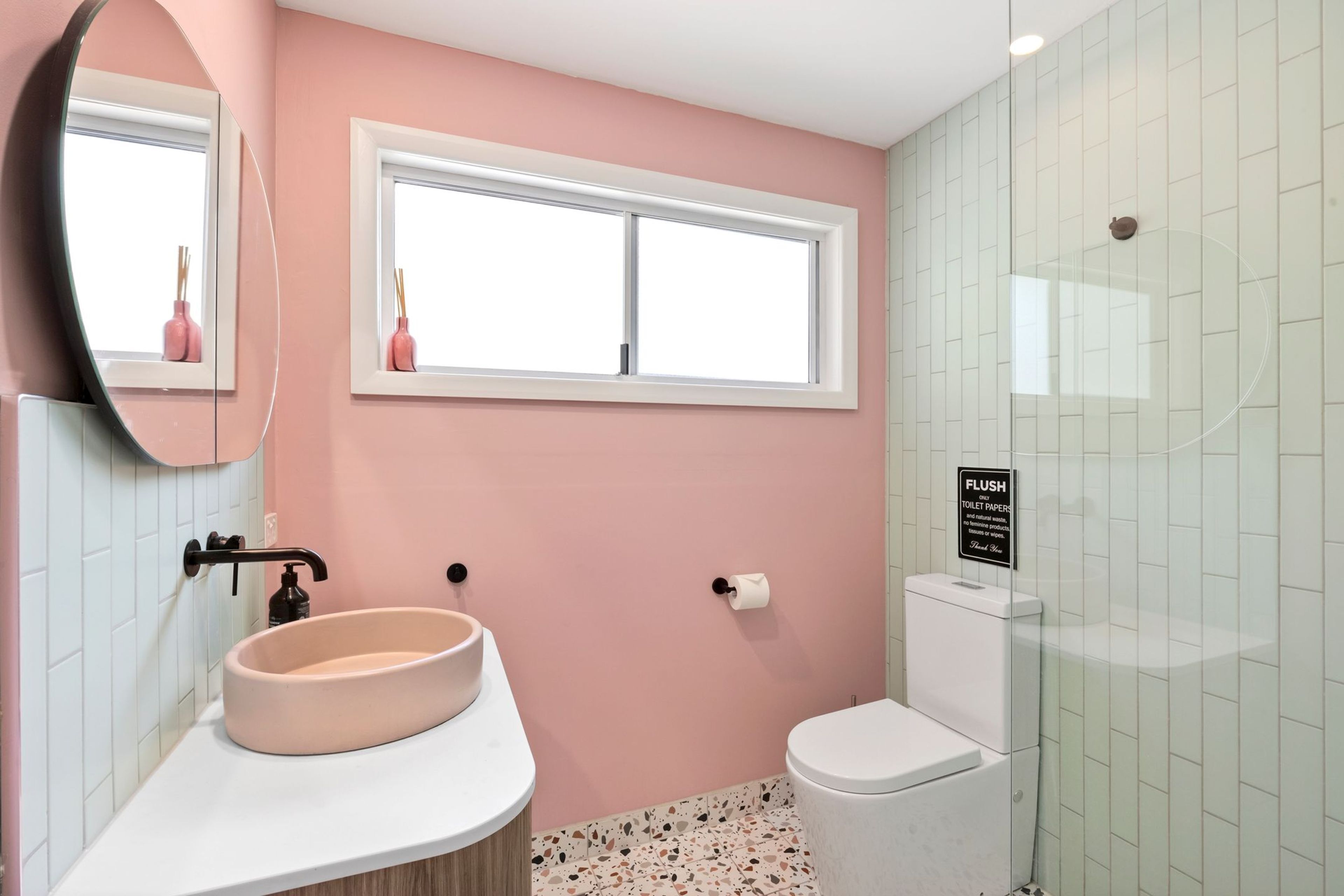 A bathroom with a pink wall, a white sink, a toilet, and a window.